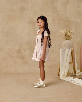 Noralee Gabrielle Dress - Rose
Young girl in a light dress standing against a beige wall with a stool and vase in the background.