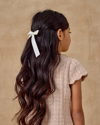 Noralee Gabrielle Dress - Rose
Person with long, wavy hair tied back with a white ribbon against a beige background