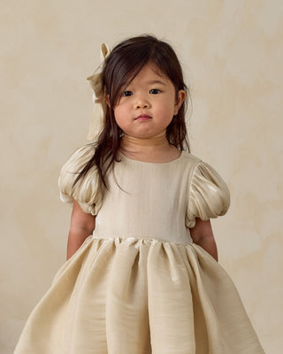 Noralee Sofia Dress - Ecru
Young girl wearing a beige dress with puffed sleeves against a plain background