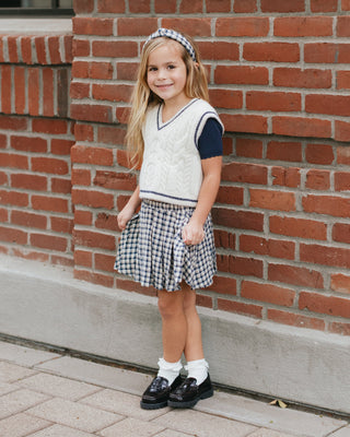 Rylee & Cru Pleated Mini Skirt - Navy Check
Young girl in a checkered dress and sweater standing against a brick wall.