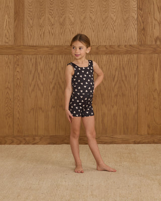 Play by Rylee & Cru Malibu Bodysuit - Hearts
Young girl wearing a black dress with white patterns against a wooden paneled wall.