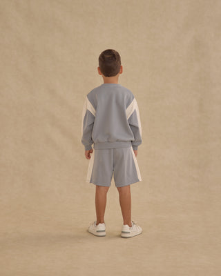 Play by Rylee & Cru Relaxed Sweatshirt - Dusty Blue
Child wearing a light blue tracksuit with white stripes on a beige background