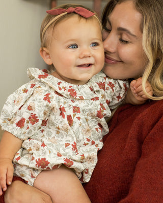 Rylee & Cru Lula Romper - Holiday Floral
Woman holding a baby wearing a floral outfit with a red headband.