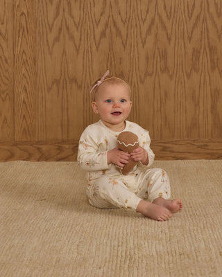 Rylee & Cru Henley Jumpsuit - Nutcracker
Baby sitting on a textured rug holding a brown toy against a wooden paneled wall.