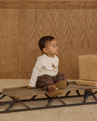 Rylee & Cru Long Sleeve Tee - Oh What Fun
Child sitting on a wooden bench against a wooden wall.