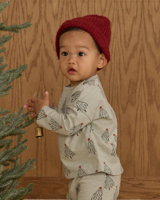 Rylee & Cru Long Sleeve Tee + Pant Set - Trees
Child wearing a red knit hat and patterned outfit standing next to a Christmas tree against a wooden wall.