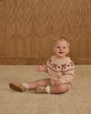 Rylee & Cru Fairisle Sweater - Bows
Baby sitting on a textured surface wearing a patterned sweater against a wooden paneled wall.