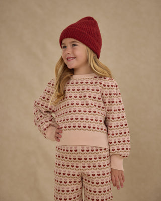 Rylee & Cru Jacquard Knit Set - Ruby Hearts
Child wearing a patterned sweater and pants with a red knit hat on a beige background