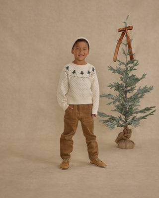 Rylee & Cru Fairisle Sweater - Trees
Child wearing a white sweater with tree pattern and brown pants standing next to a small decorated Christmas tree on a beige background.