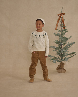 Rylee & Cru Fairisle Sweater - Trees
Child wearing a patterned sweater and brown pants standing next to a small Christmas tree on a beige background