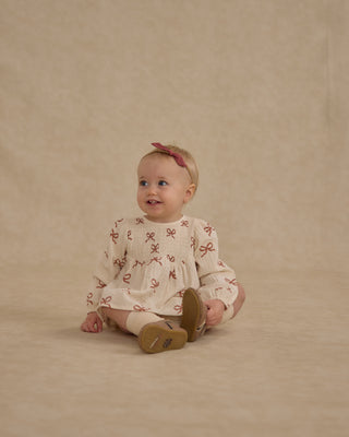 Rylee & Cru Sophia Top + Bloomer Set - Ruby Bows
Baby sitting on a beige background wearing a cream outfit with red patterns
