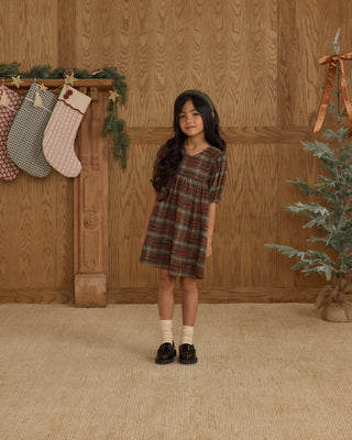 Rylee & Cru Jolene Dress - Holiday Plaid
Young girl in a plaid dress standing in front of a wooden wall with Christmas stockings and decorations.