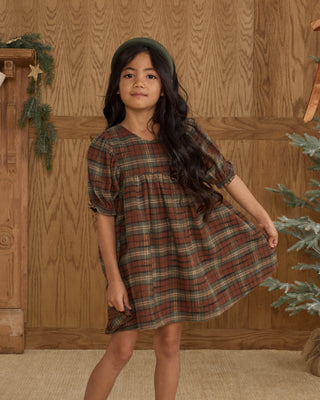 Rylee & Cru Jolene Dress - Holiday Plaid
Young girl wearing a plaid dress standing in front of a wooden wall with Christmas decorations.
