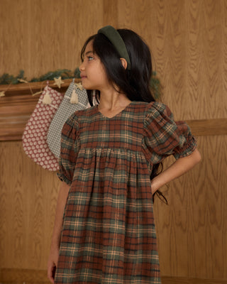Rylee & Cru Jolene Dress - Holiday Plaid
Young girl wearing a plaid dress with a wooden wall background