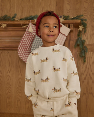 Rylee & Cru Relaxed Sweatshirt & Jogger Sweatpant Set - Christmas Dogs
Child wearing a cream-colored outfit with dog pattern in front of a wooden wall with Christmas decorations.