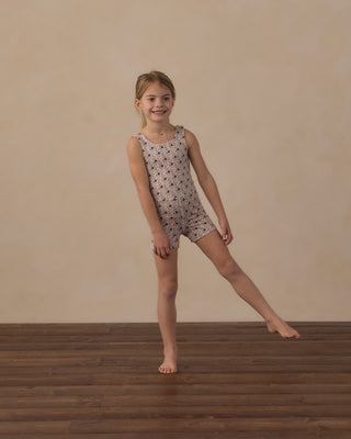 Play by Rylee & Cru Malibu Bodysuit - Blue Primrose
A young girl stands barefoot on a wooden floor against a beige wall, wearing a sleeveless one-piece leotard with a small repeating black pattern on a light beige or off-white base.