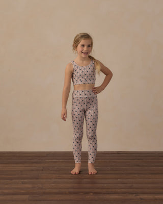 Play by Rylee & Cru Swift Sports Bra - Blue Primrose
Play by Rylee & Cru Basic Legging - Blue Primrose
A young girl stands barefoot in a studio wearing a matching two-piece outfit with a small black floral pattern on a light beige fabric. The set includes a sleeveless crop top and high-waisted leggings, set against a plain beige wall and dark wood floor.
