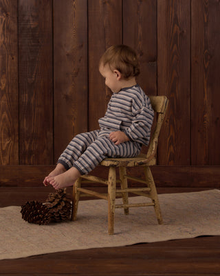 Rylee & Cru Relaxed Set - Blue Stripe
A toddler wearing a matching striped long-sleeve top and pants set sits on a small rustic wooden chair in front of a dark wood plank wall. The outfit has thin dark stripes on a light gray or off-white base.