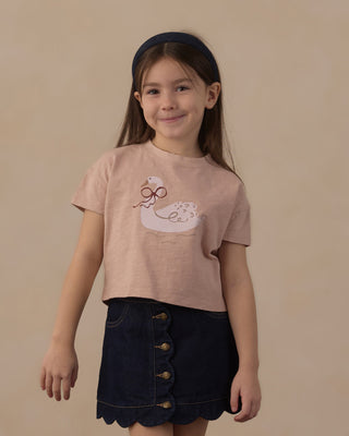 Rylee & Cru Scallop Mini Skirt - Dark Indigo
A young girl with a dark navy blue headband is wearing a light pink short-sleeve t-shirt with a white duck graphic and a dark navy blue denim skirt. She is standing against a solid beige studio background.