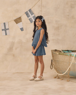 Rylee & Cru Faye Set - Marine
Young girl in a denim dress standing next to a vintage bassinet with decorative flags on a beige wall.