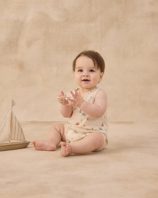Rylee & Cru Sleeveless One-Piece - Aquatic
Baby sitting on a beige blanket with a toy boat, wearing a floral romper.