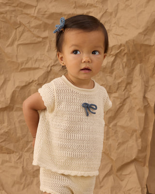 Rylee & Cru Crochet Bow Clip Set - Marine
Rylee & Cru Scallop Knit Baby Set - Natural
Baby wearing a beige knitted outfit with a blue bow against a brown textured background