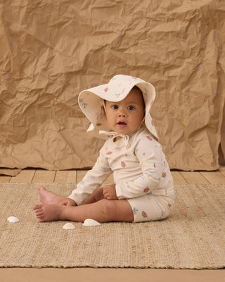 Rylee & Cru Floppy Swim Hat - Aquatic
Baby sitting on a woven mat wearing a floral outfit and sun hat against a textured brown backdrop.
