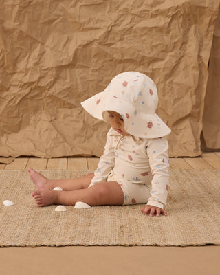 Rylee & Cru Floppy Swim Hat - Aquatic
Child wearing a floral sun hat and outfit sitting on a textured surface with a brown backdrop