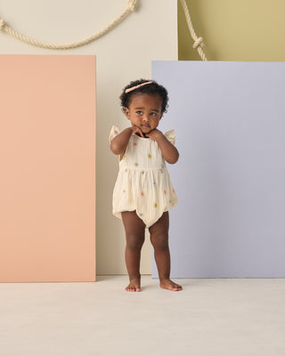 Rylee & Cru Amelia Romper - Embroidered Daisies
Baby in a white romper with floral patterns standing against a colorful background