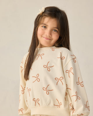 Rylee & Cru Summer Terry Set - Sailor Bows
Young girl wearing a cream sweater with bow patterns on a plain background