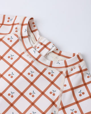 Rylee & Cru Delphine Cherry Check rashguard one-piece swimsuit for girls, featuring a playful cherry check pattern and long sleeves.