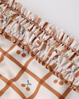 Rylee & Cru Rouched Bikini - Cherry Check
Close-up of a fabric with ruffled edge and brown grid pattern on a white background