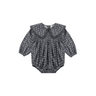 Rylee & Cru Fern Romper - Heart Ditsy
A baby girl's long-sleeve romper in a dark gray and white floral print, featuring a wide ruffled Peter Pan collar and a smocked bodice, shown flat on a white background.