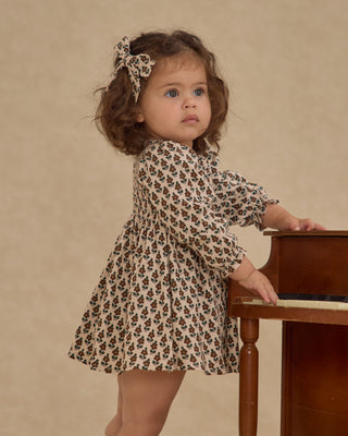 Rylee & Cru Capri Dress - Harvest Floral
Child wearing a patterned dress standing next to a wooden chair against a beige background