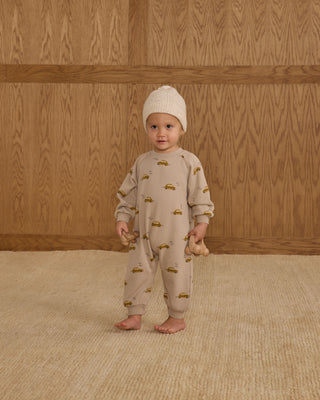 Rylee & Cru Raglan Jumpsuit - Taxi
Baby in a beige onesie with car pattern standing against a wooden wall.