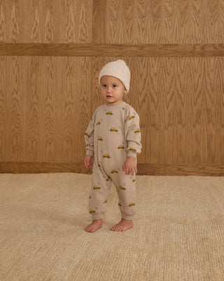 Rylee & Cru Raglan Jumpsuit - Taxi
Baby in beige pajamas with car pattern standing against a wooden wall.
