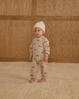Rylee & Cru Raglan Jumpsuit - Taxi
Baby in a beige outfit with vehicle pattern standing against a wooden paneled wall.