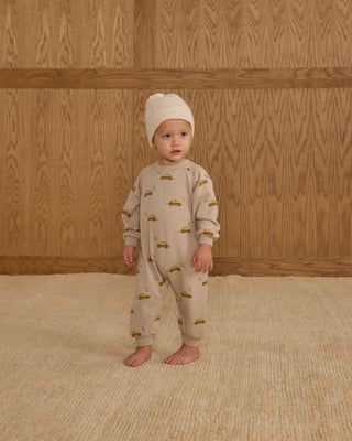 Rylee & Cru Raglan Jumpsuit - Taxi
Baby wearing a beige onesie with car prints and a matching hat, standing against a wooden paneled wall.