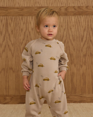 Rylee & Cru Raglan Jumpsuit - Taxi
Child wearing a beige onesie with car patterns against a wooden background