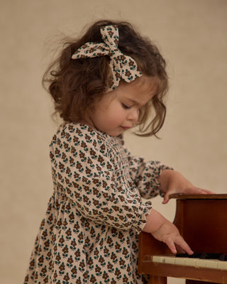 Rylee & Cru Bow - Harvest Floral
Child wearing a floral dress and headband, interacting with a wooden object against a beige background