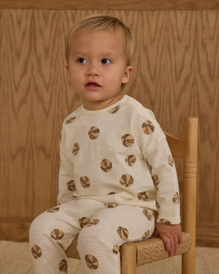 Rylee & Cru Long Sleeve Tee + Pant Set - Basketball
Child wearing a white outfit with brown patterns sitting on a wooden chair against a wooden wall.