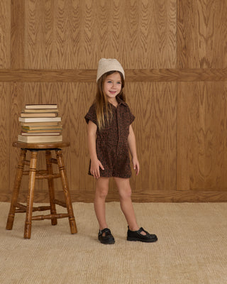 Rylee & Cru Utility Romper - Leopard
Young girl in a brown dress and white hat standing next to a stack of books on a wooden stool against a wooden paneled wall.