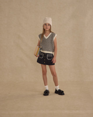 Rylee & Cru Sweater Vest - Black Speckle
Young girl wearing a patterned sleeveless top and denim skirt on a beige background
