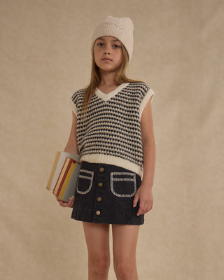 Rylee & Cru Sweater Vest - Black Speckle
Young girl wearing a patterned sleeveless top and skirt, holding books against a beige background