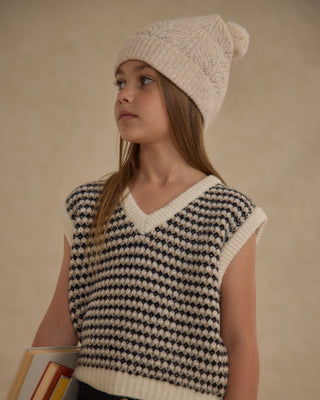 Rylee & Cru Sweater Vest - Black Speckle
Young girl wearing a knitted sleeveless vest and hat against a beige background