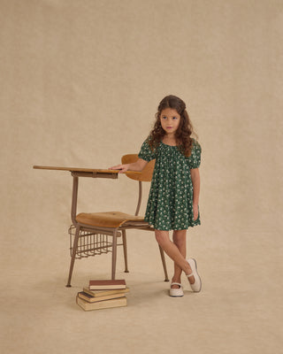 Rylee & Cru Sabrina Mini Dress - Green Ditsy
Young girl in a green dress standing next to a vintage desk and chair on a beige background