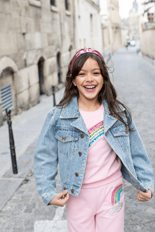 Lola and The Boys Rainbow Dreams Joggers Set
Young girl in a denim jacket and pink outfit with rainbow details on a street.
