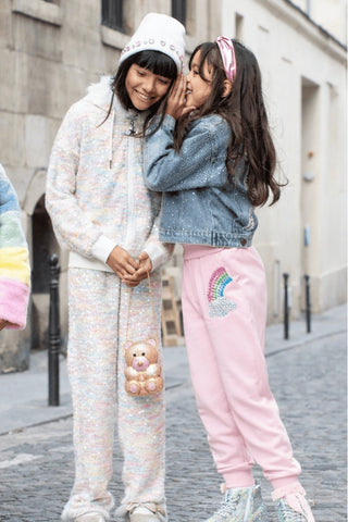 Lola and The Boys Rainbow Dreams Joggers Set
Two children on a street, one in pastel pajamas with a teddy bear, the other in pink rainbow pants and denim jacket.