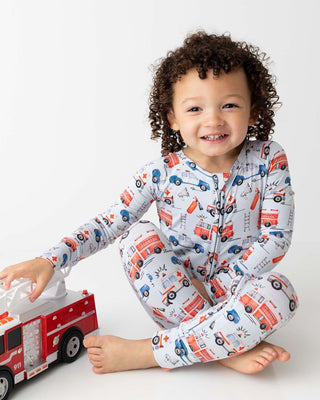 Lev Baby Poppy Convertible Zipper Romper - Ryan
Child wearing a pajama with vehicle pattern, sitting with a toy fire truck on a white background