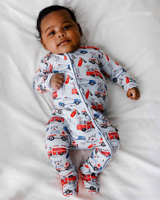Lev Baby Zippered Footie - Ryan
Baby wearing a onesie with fire truck and car patterns on a white blanket